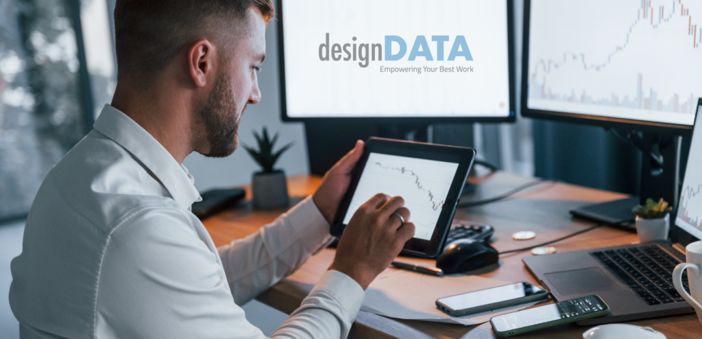 A professional man analyzes data on a tablet, sitting at a desk surrounded by multiple screens displaying graphs.