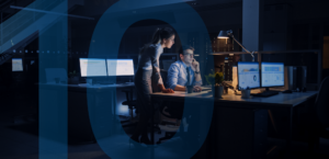 A man and a woman in a dark, modern office environment, analyzing data on multiple computer screens late at night. The man is seated and the woman stands next to him, both focused intently on the monitors displaying graphs and analytics. There is a blue number 10 laid on top of the image.