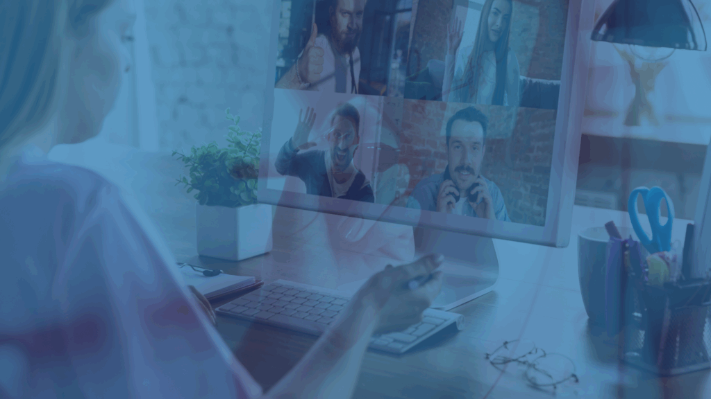 A person sitting at a desk on a video call with four team members, each shown in separate windows on a computer monitor.